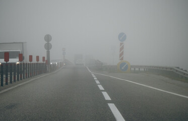 Fototapeta premium Foggy road with cars and warning signs in low visibility.