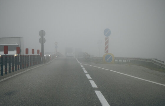 Foggy road with cars and warning signs in low visibility.