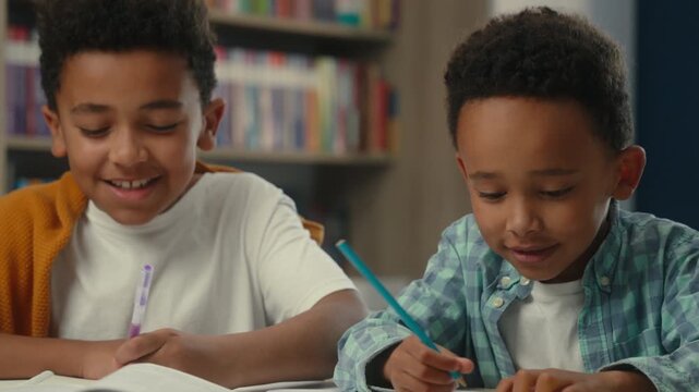 Close up happy smiling laughing kids African American little boys writing homework learning languages study math cheerful brothers schoolboys school children write joyful studying primary knowledge