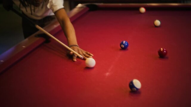 Tilt down shot of young adult African American man aiming cue then sinking shot in pool game on table with red cloth while relaxing with female friend at billiard hall