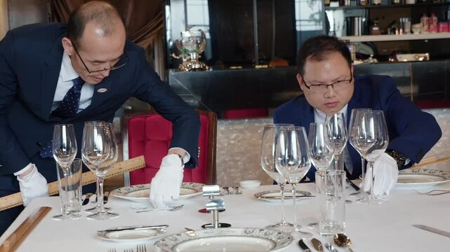 Two professional waiters in white gloves meticulously preparing a table for fine dining service