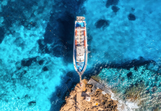 Aerial view of boat with people and rocky sea coast on sunny summer day. Top drone view of yacht, transparent azure water, path. Mediterranean sea. Travel in Sardinia island, Italy. Tropical landscape