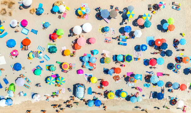 Aerial view of colorful umbrellas on sandy beach, relaxing people near blue sea on sunny summer day. Sardinia, Italy. Tropical landscape. Travel and vacation. Top down view. Concept