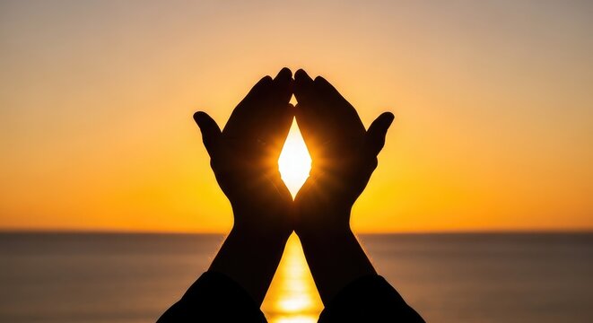 Silhouetted hands praying towards a brilliant sunset over the ocean