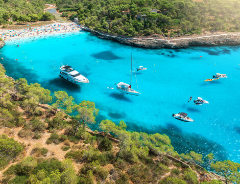 Aerial drone view of yachts and boats anchored in turquoise sea bay surrounded by rocky coastline and pine forest, summer vacation scene near Cala Mondrago, Mallorca, Balearic Islands, Spain. Top view