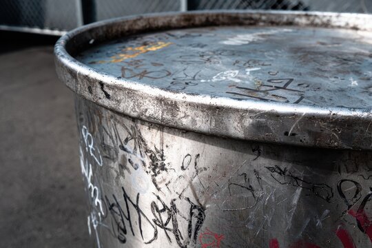 Heavily dented and scratched metallic trash can surface urban vandalism texture.