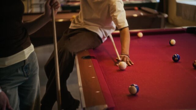 Tilt down shot of smiling young adult Black man taking challenging shot on pool table during casual get together with female friend at billiard hall