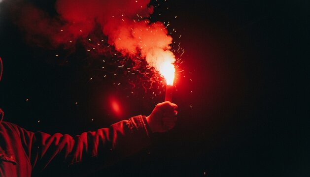 A close-up shot of a hand holding a glowing red emergency flare against a dark, night-time background with smoke and embers.