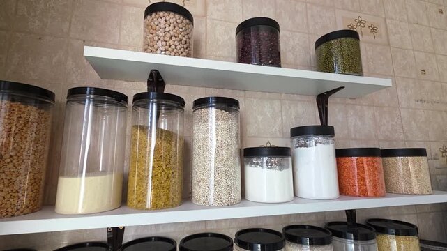 Kitchen pantry shelves filled with various legumes, grains, and flour stored in transparent containers, presenting an organized and practical kitchen storage solution