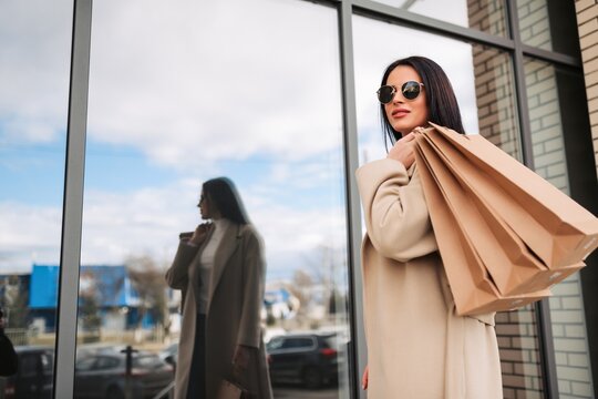 Stylish woman carrying shopping bags outside a glass storefront on a crisp city day