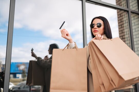 Stylish young woman holding shopping bags and credit card outside a retail store window