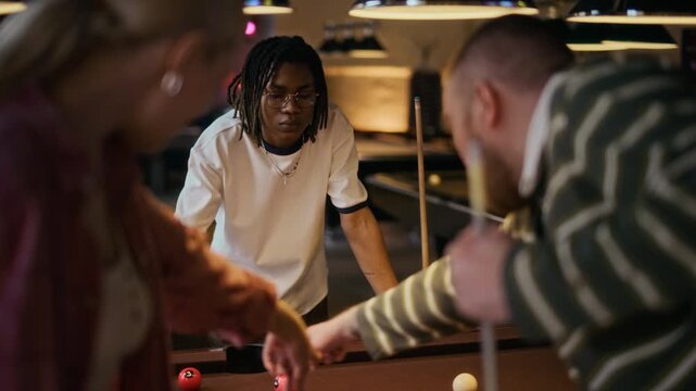 Focused young adult African American man thinking over billiards strategy while discussing table layout with friends at pool club