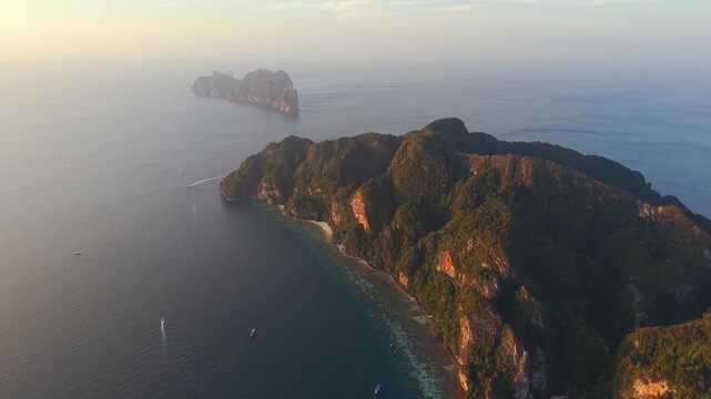 Drone sunset shot of Koh Phi Phi cliffs and coastline with golden light and calm sea, stunning aerial view.