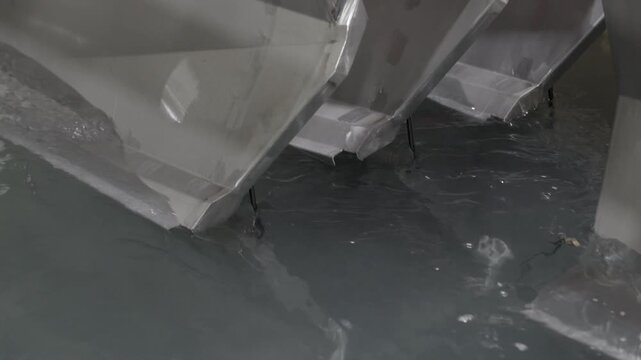 Close-up footage of metal sheets being immersed into a coating bath during the KTL coating (cathodic dip coating) process. The camera captures the moment of entry into the liquid, highlighting surface