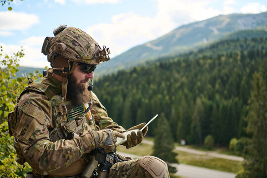 Tactical Soldier Using Tablet and Radio Communications While On Patrol in Forested Mountain Terrain