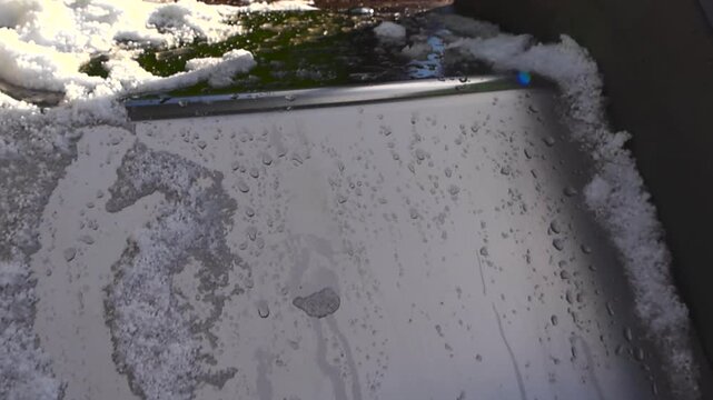 Close up view of snow melting on a metal playground slide during a sunny winter day, with water drops forming and trickling down, signifying the transition from winter to spring