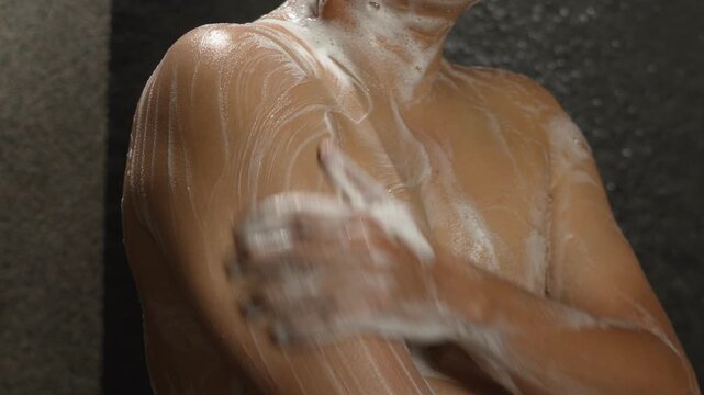 A man bathes in the bathroom rubbing the gel over his body. washes head and body in shower. washing foaming cleaning of hair, head, scalp.	