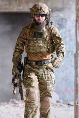 Obraz premium Armed Tactical Soldier in Multicam Gear Walking Through Urban Ruins With Helmet and Rifle