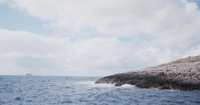 Waves Crashing Against Rocky Coastline with Distant Island on Horizon Under Cloudy Sky