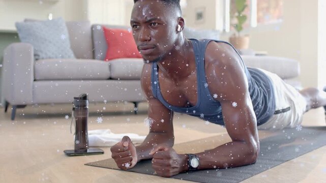 Man starting forearm plank on mat holding core while snow particles drifting around him for fitness