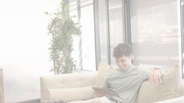 Man entering frame with tablet, sitting on beige sofa, tapping and swiping for tech demo