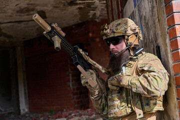Obraz premium Bearded Soldier in Tactical Gear With Rifle Conducting Urban Military Operation in Ruined Building