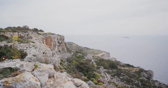 Scenic coastal view of rugged limestone cliffs and the sea under an overcast sky, with a distant small island