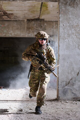 Obraz premium Soldier in Tactical Gear Running With Rifle Inside Abandoned Building During Urban Combat Training