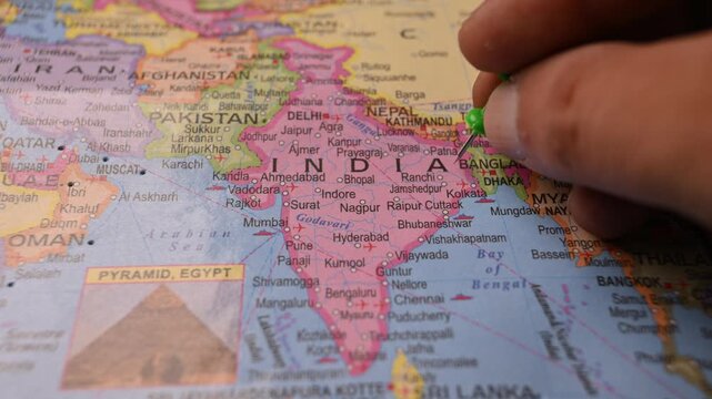 Man Pointing Green Pin on India Location on Paper World Map Close Up
