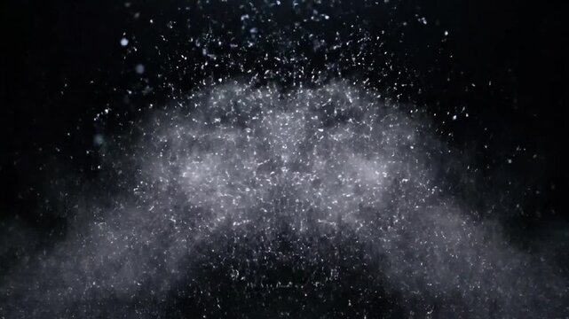 Particles explode outward in a dynamic burst of white powder against a dark background
