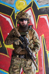 Obraz premium Armed Tactical Soldier In Camouflage Gear With Rifle Posing Against Urban Graffiti Wall