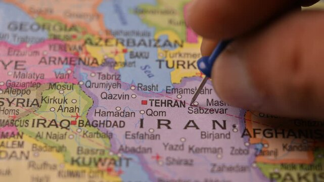 Man Pointing Blue Pin on Tehran Iran Location on Paper World Map Close Up