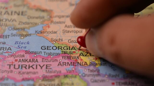 Man Pointing Red Pin on Georgia Location on Paper World Map Close Up