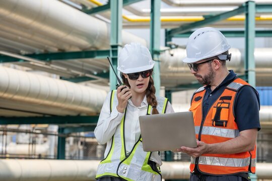 Male and female petroleum engineers in safety uniform pointing while discussing about maintenance project under oil pipeline system at fuel refinery plant engineering teamwork energy industry.