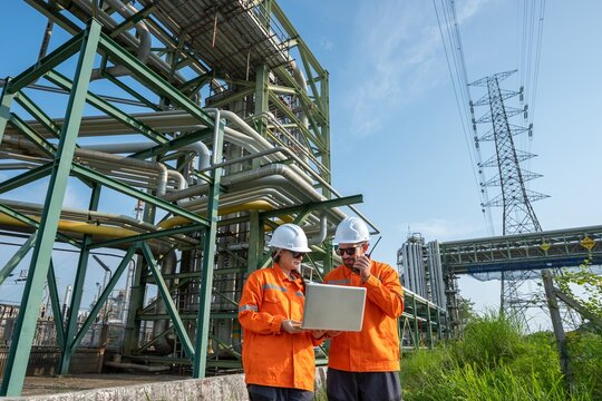 Male and female petroleum engineers in safety uniform pointing while discussing about maintenance project under oil pipeline system at fuel refinery plant engineering teamwork energy industry.