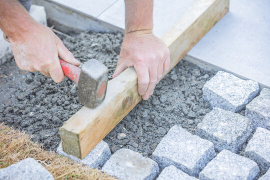 Worker installing cobblestone pavement with hammer and wooden guide