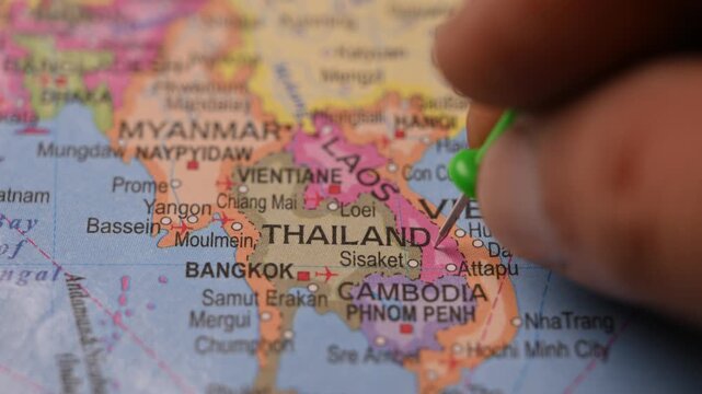 Man Pointing Green Pin on Thailand Location on Paper World Map Close Up