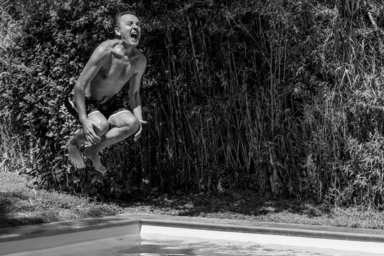 A man dives into a pool surrounded by tall cane and bamboo plants, in black and white