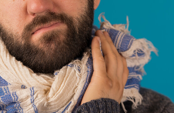 Close-up of a man with a beard, wearing a scarf and touching his face. Represents comfort and warmth