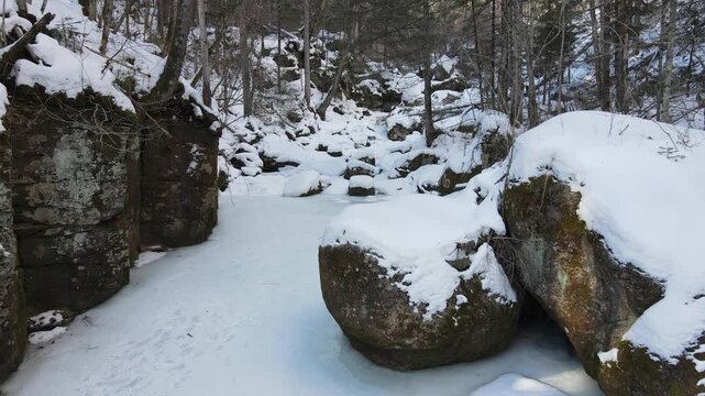 A peaceful and remote winter landscape featuring snow-covered trees, frozen sections of a river, and a winding path marked with many human footprints.