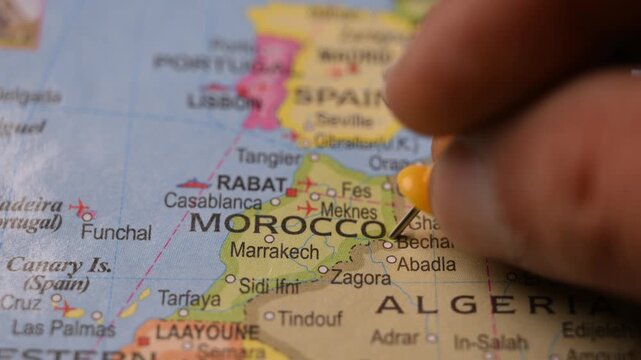 Man Pointing Yellow Pin on Morocco Location on Paper World Map Close Up