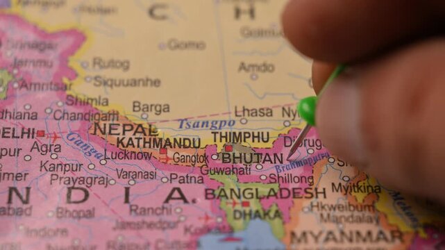 Close Up of Man Pointing Green Location Pin on Bhutan in Paper World Map Travel Concept