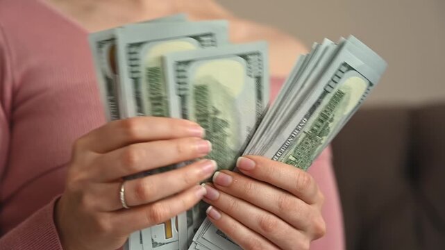 Woman hands counting stack of hundred dollar bills in slow motion close up footage of cash movement.
