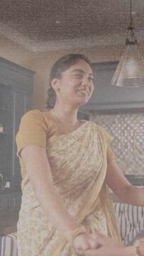 Vertical video: Mom and daughter clasping hands, turning in kitchen sharing home joy in sarees