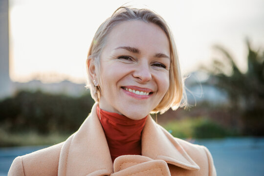 Portrait of young caucasian woman smiling outdoors. Confident headshot of mid adult female looking at camera standing outside