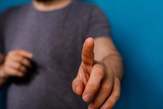 Close up of a man's hand pointing at something with his index finger against a blue backg