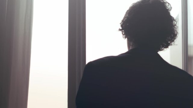 Young man closing window and blinds in soft daylight scene