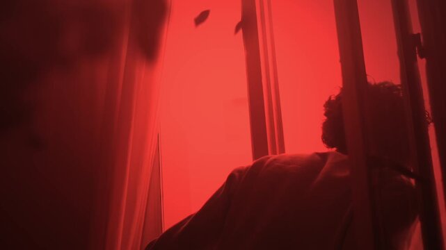 Man opening window under red light checking outside danger