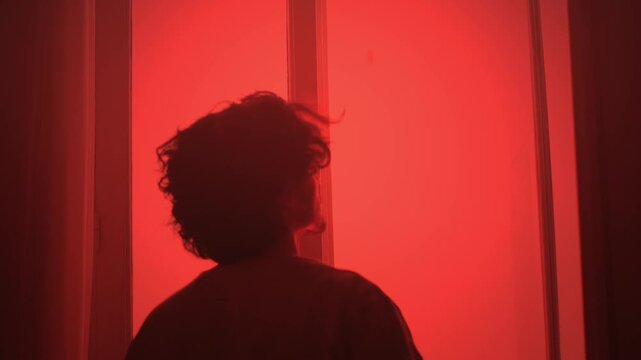 Man closing window under red light in tense alert atmosphere