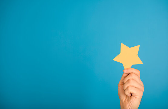 Hand holding yellow star against a blue background, representing achievement and success.